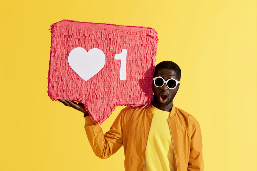 A man with a surprised look on his face holds up a piñata that resembles the Instagram heart symbol.