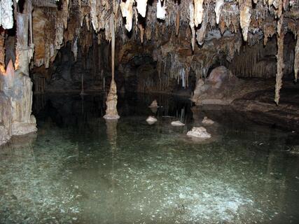 Stalactites hang over a temporary pool created by snowmelt inside one of the Lehman Caves. Several stalagmites protrude from the pool.