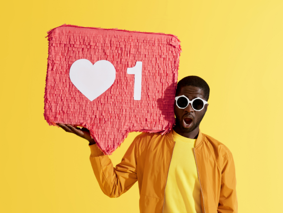 A man with a surprised look on his face holds up a piñata that resembles the Instagram heart symbol.