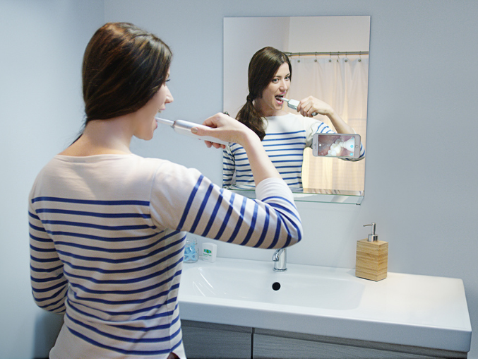 A woman brushes her teeth in front of a mirror.